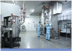 Technicians in cleanroom suits operating electrode mixing equipment